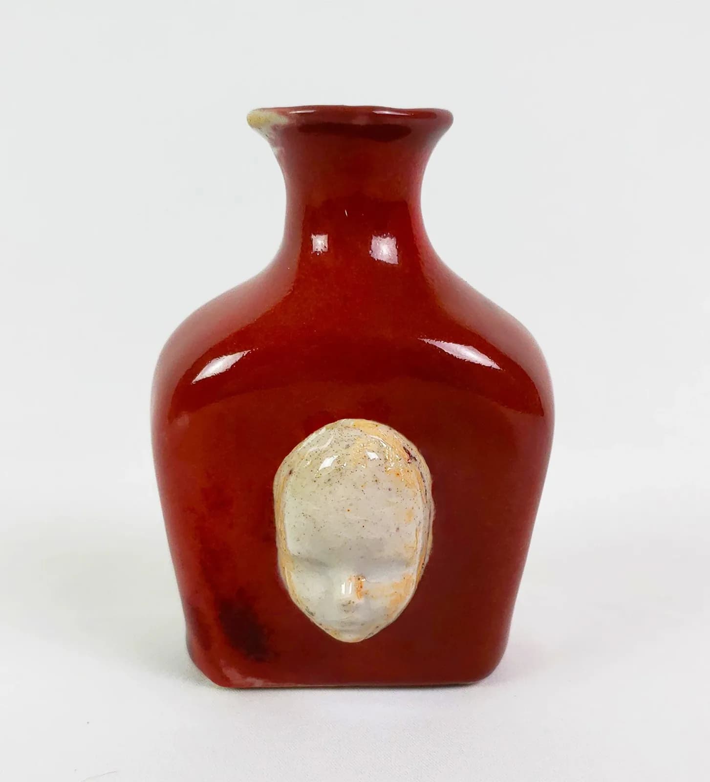 A deep-red glazed ceramic vessel with a cream-colored stone or quartz element inset on its front face.
