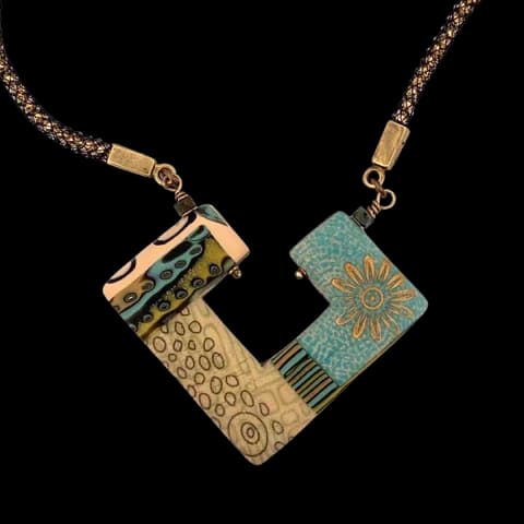 Geometric mixed-metal pendant with etched brass and patina elements on a beaded chain.