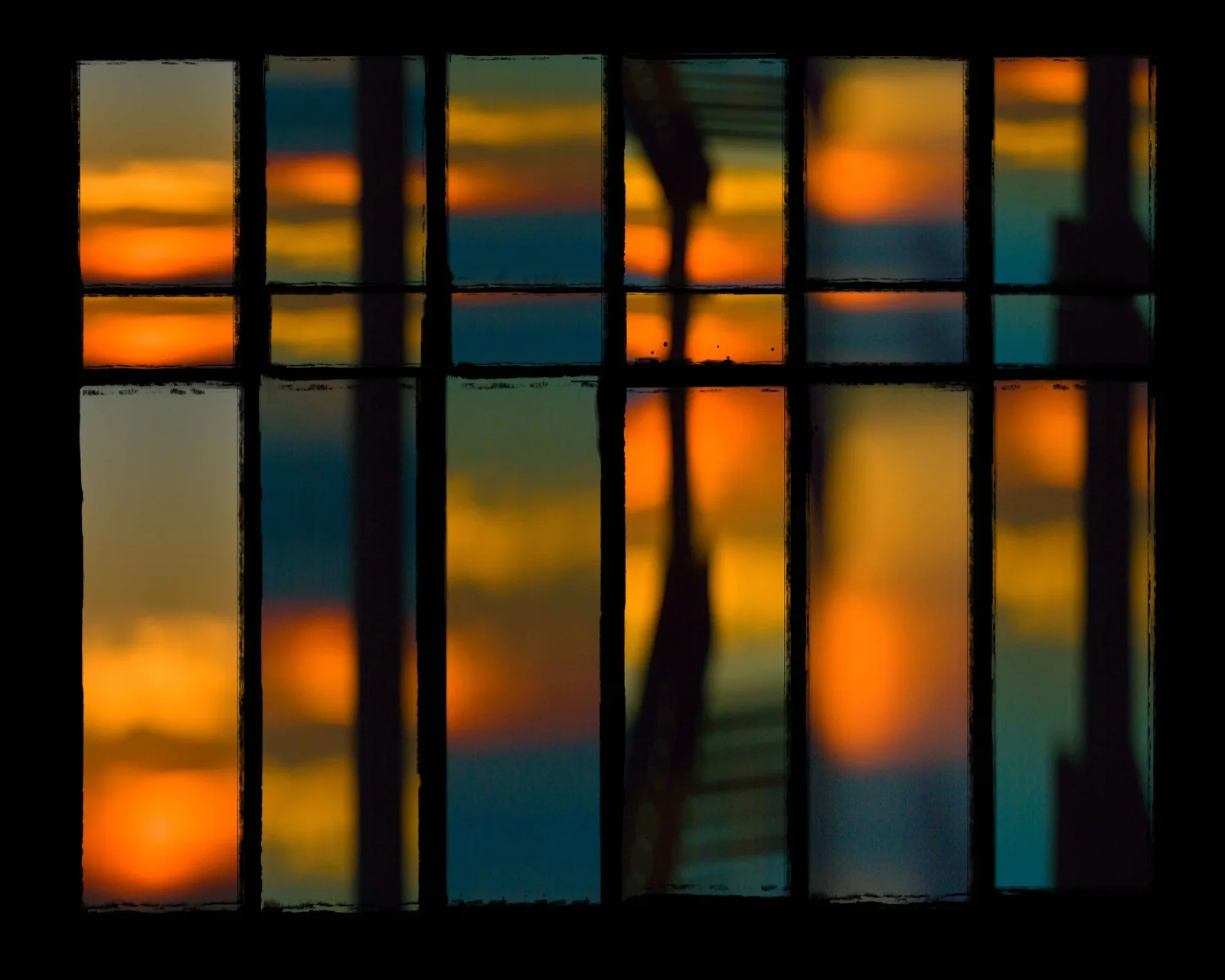 Sunset light refracted through a multi-pane window creates an abstract geometric composition in warm and cool tones.