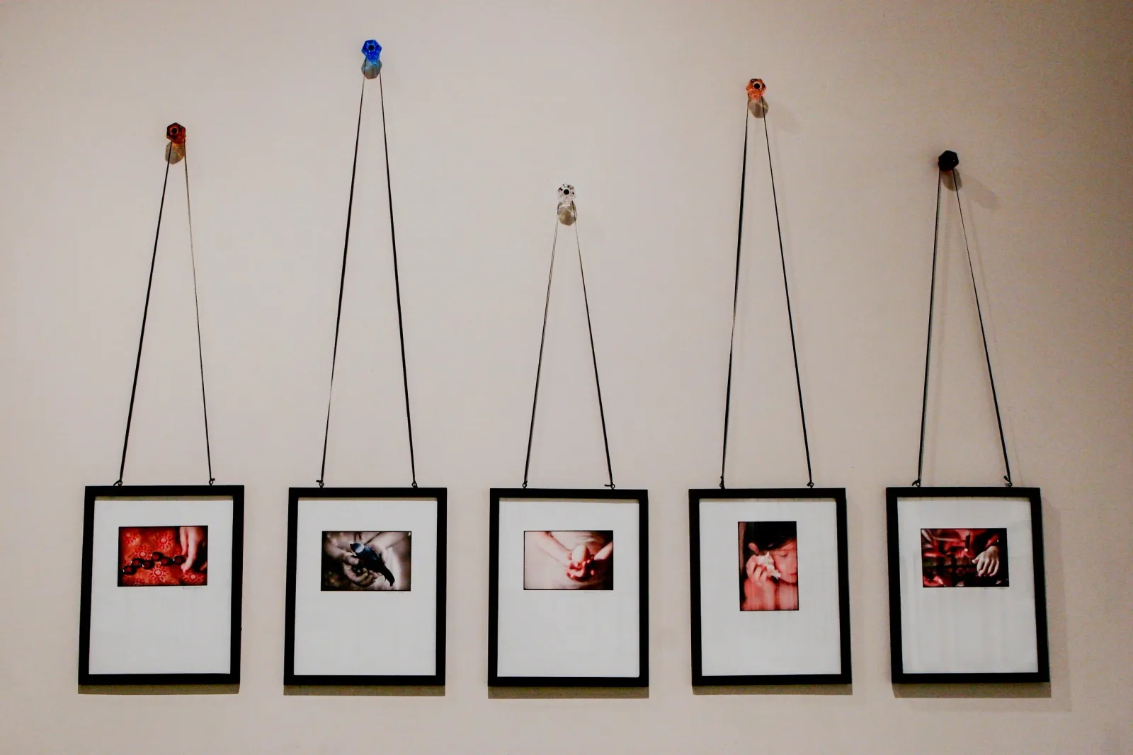 Five framed photographs suspended by string and topped with colorful beads form a cohesive wall installation.