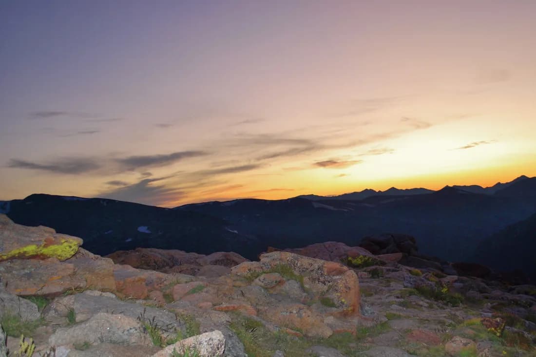 Sunset view from a Boulder ridge with distant mountain silhouettes and the Flatirons on the horizon.