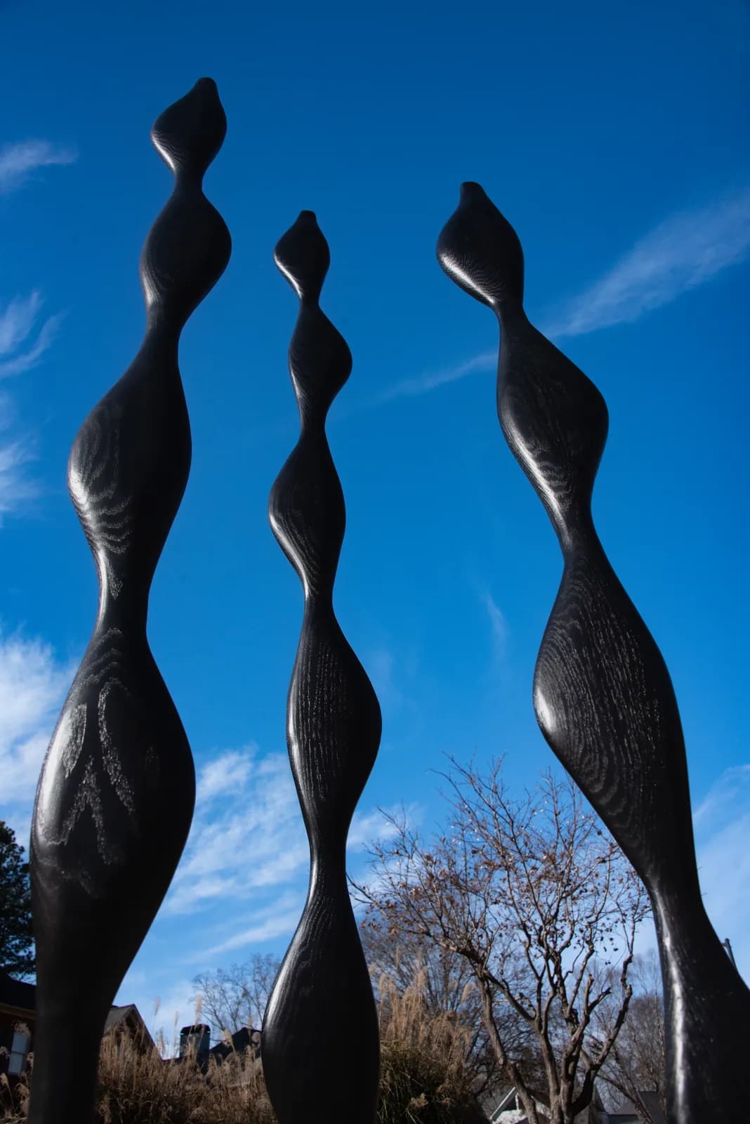 Three tall abstract bronze figures reach upward against the clear blue sky and distant Boulder Flatirons.