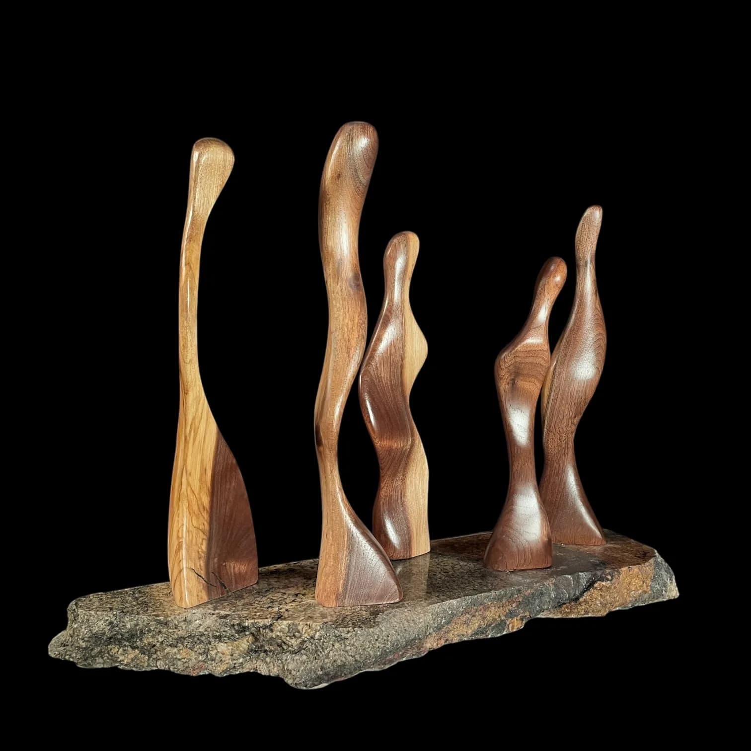 Five organic wood forms mounted on a natural stone base, carved and finished in warm wood tones.