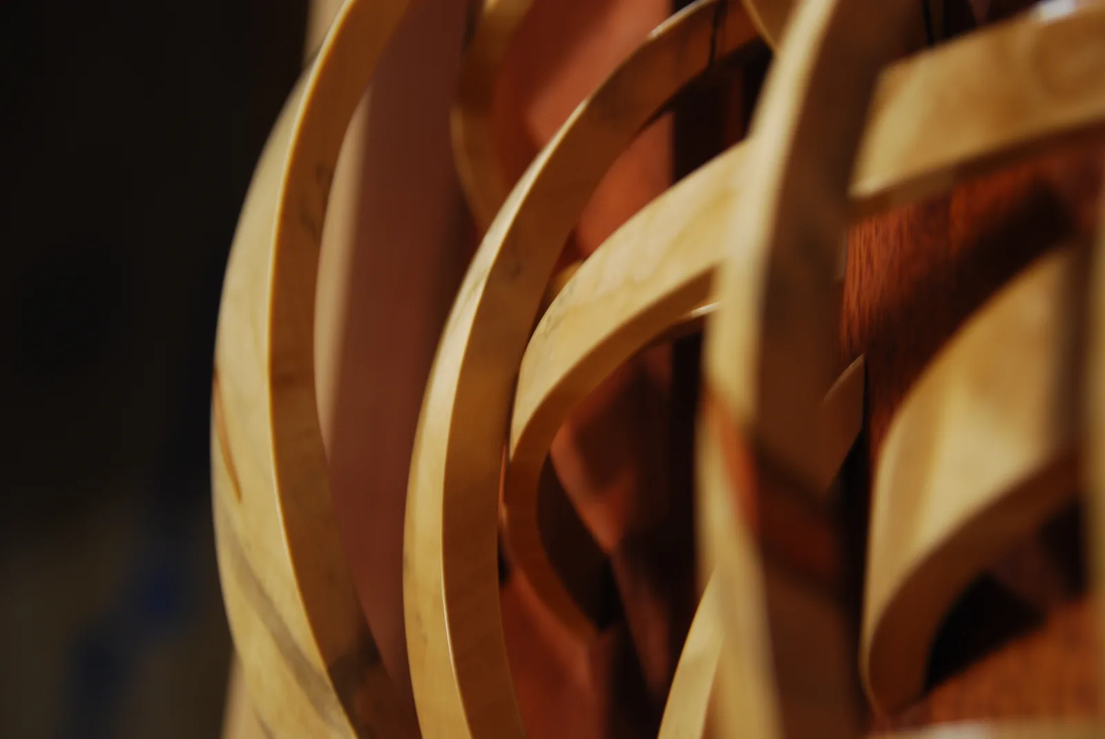 Abstract wooden sculpture with interlocking curved forms, lit to emphasize warm tones and depth.