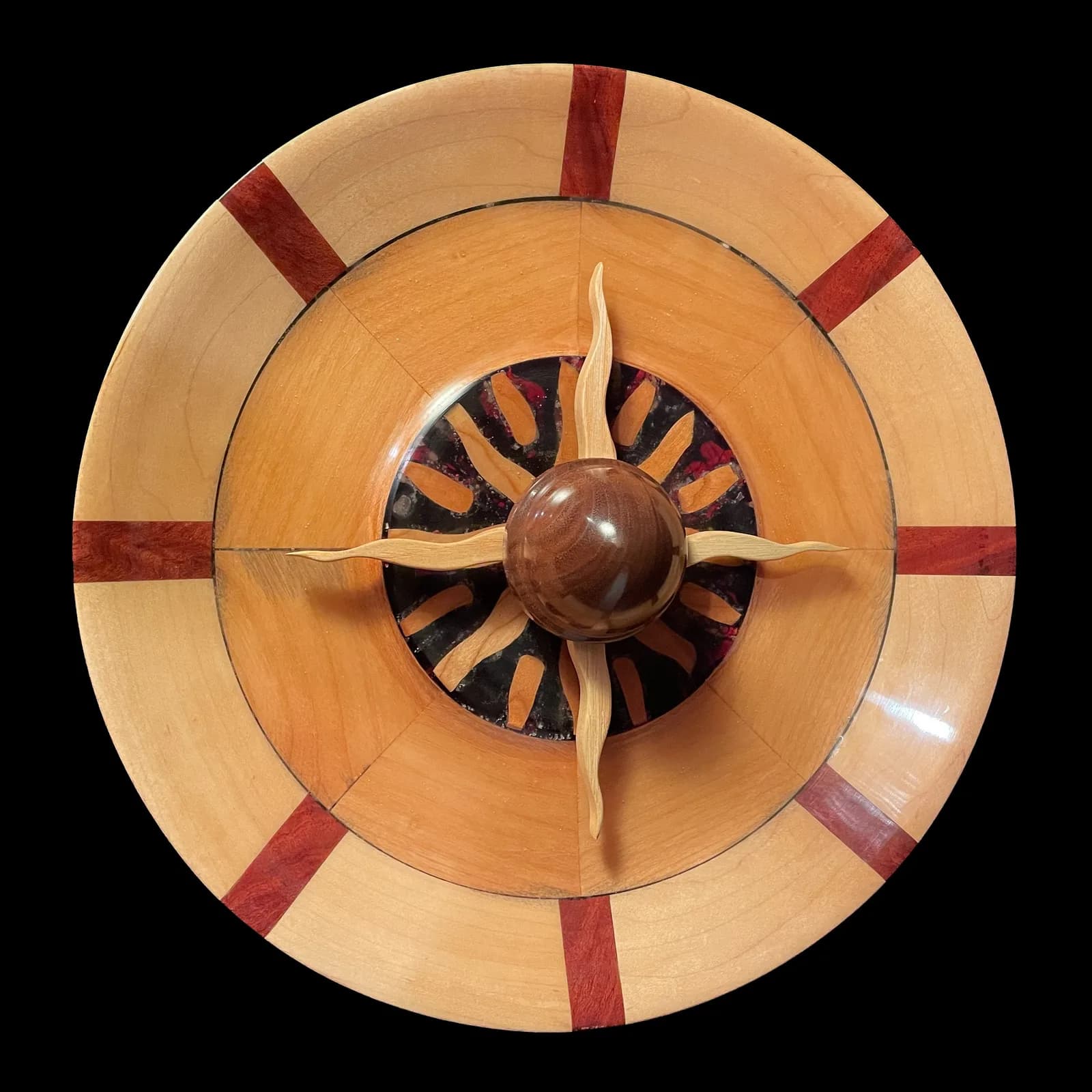 Circular wood sculpture with inlaid geometric pattern and central sphere with four-pointed blade.