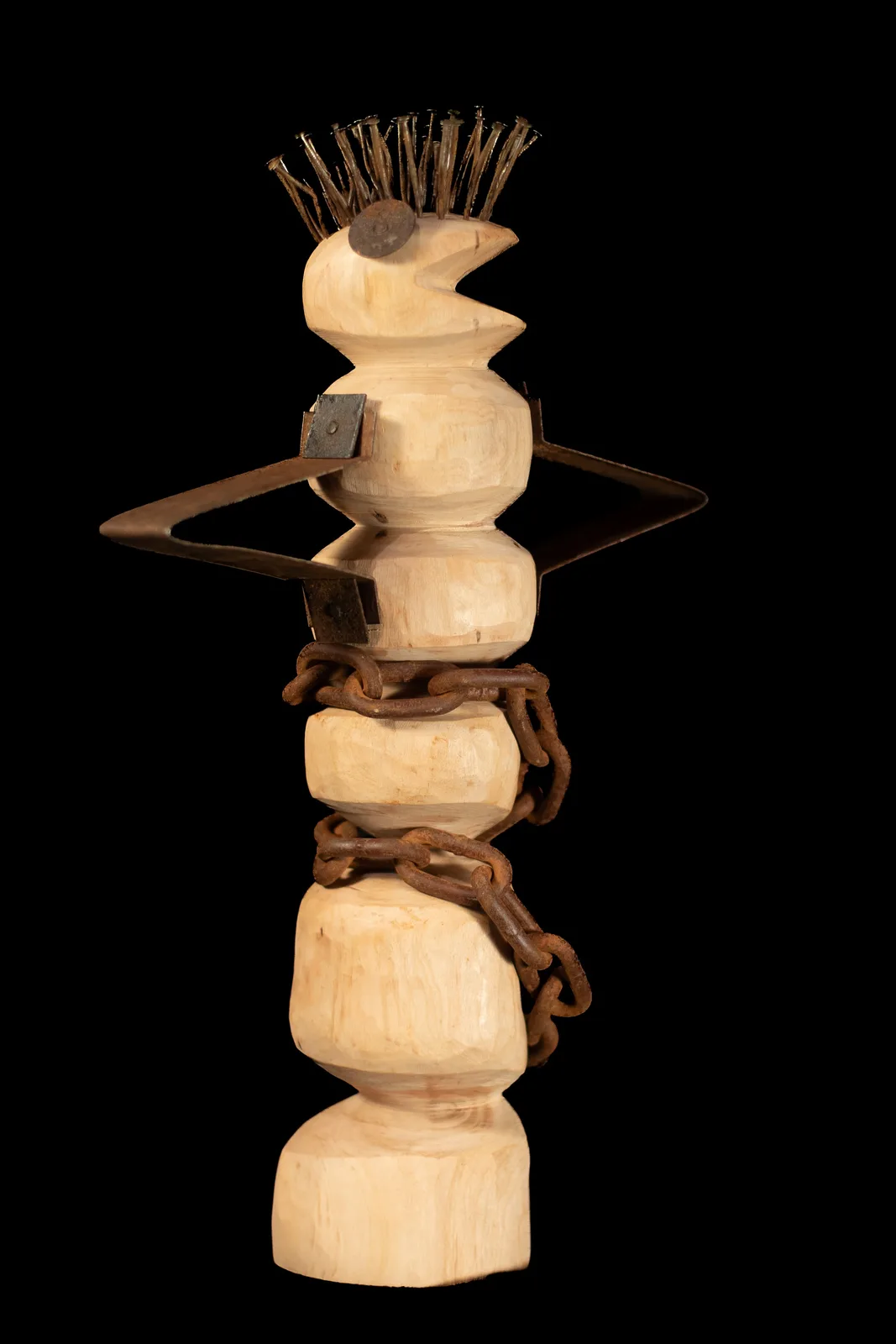 A carved wooden sculptural figure with stacked organic forms, incorporating metal elements and natural grain.