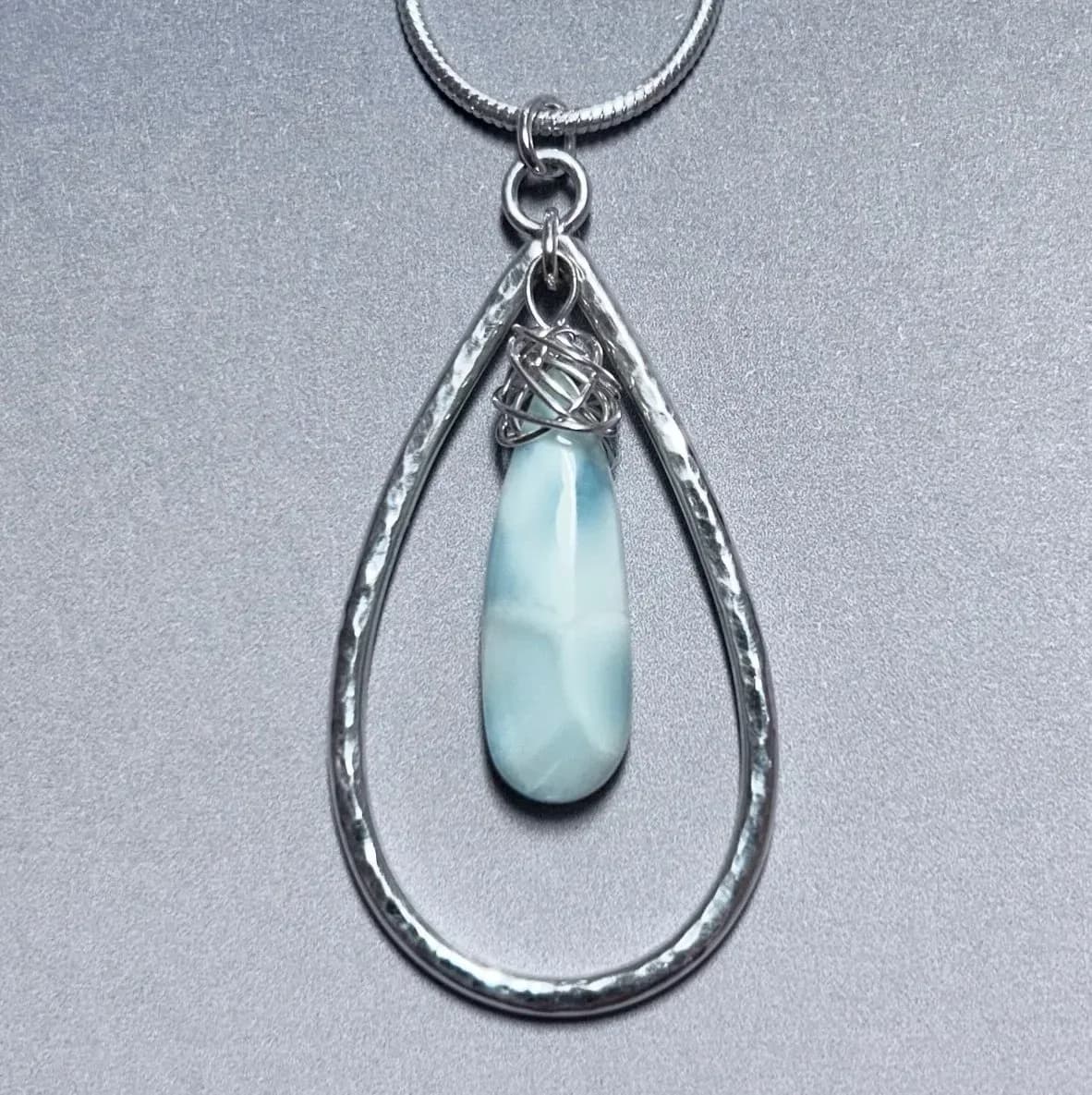 Silver teardrop pendant with pale blue-green stone on a snake chain.