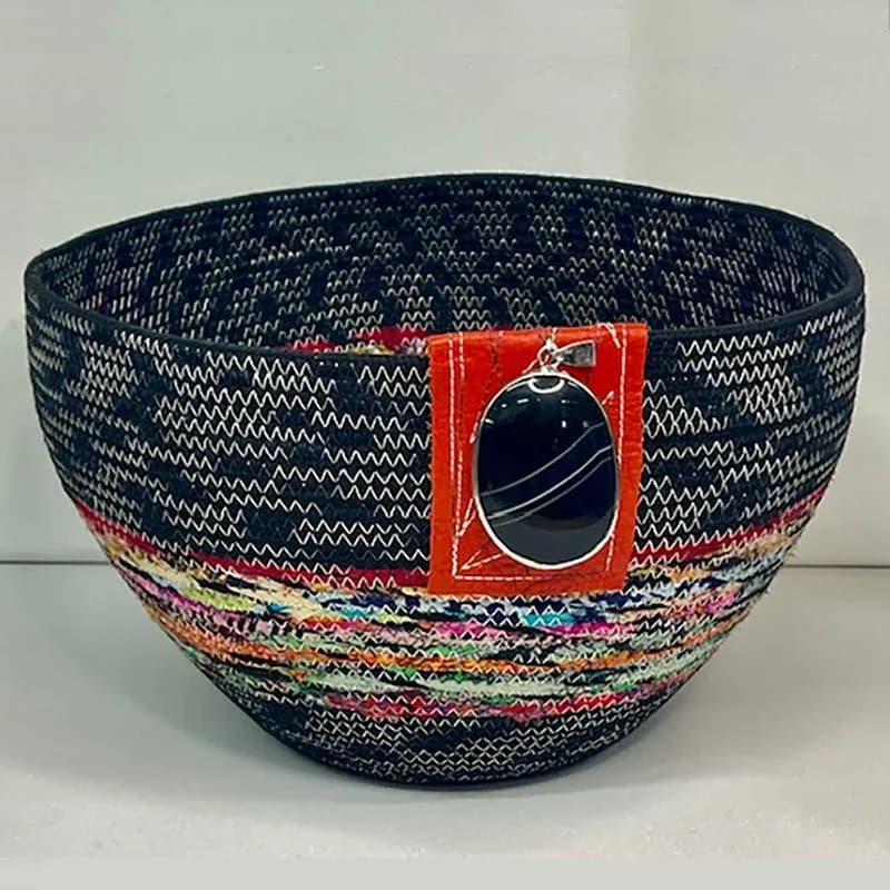 A woven fiber basket with mixed-color textile bands and a red fabric panel featuring a mirrored embellishment.