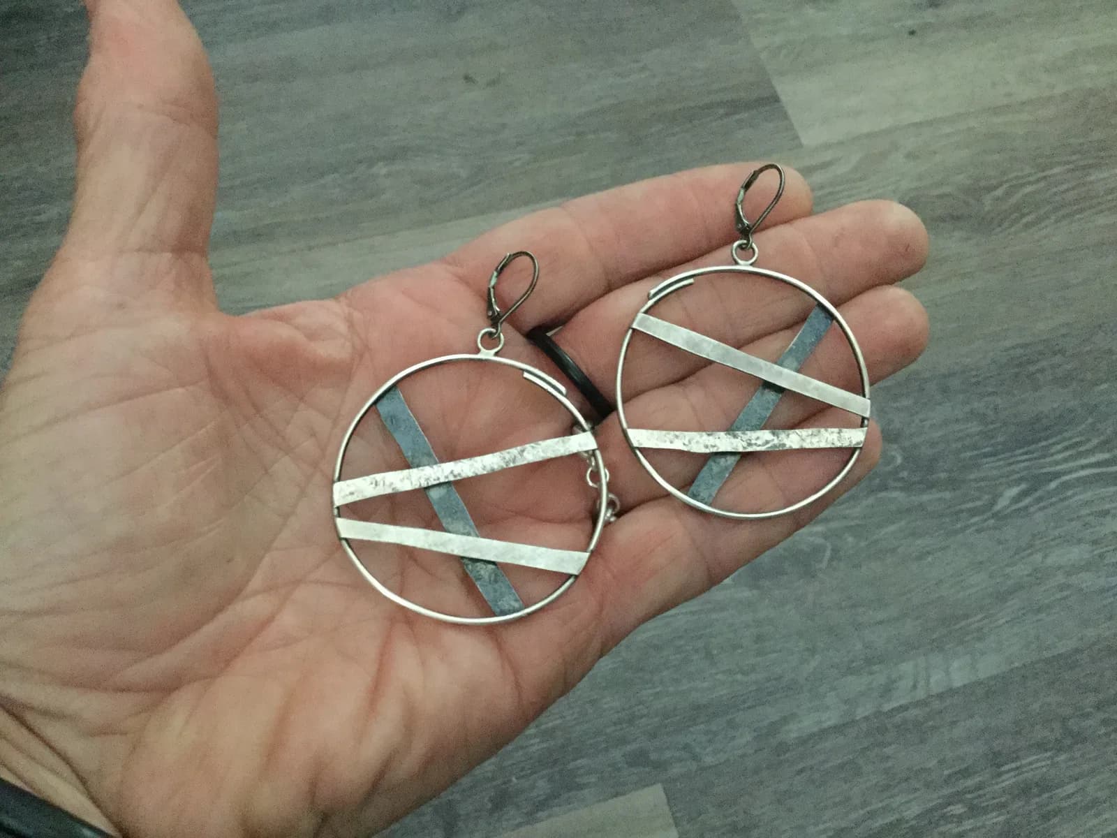 Pair of geometric circular earrings with intersecting wire and patinated metal elements.