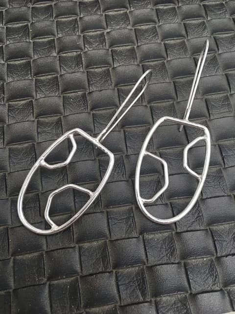 Pair of silver-toned wire earrings with organic abstract forms on textured surface.
