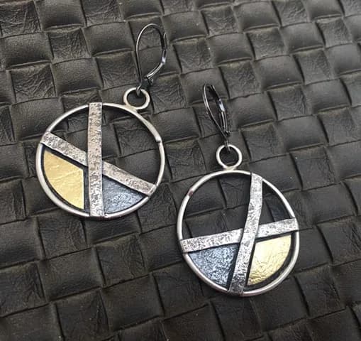 A pair of silver and brass geometric earrings with abstract crossed-line design and circular forms.