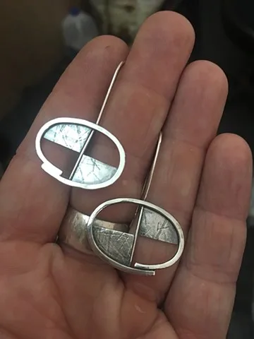 Two silver and inlay rings with geometric divided ovals in the palm of a hand.