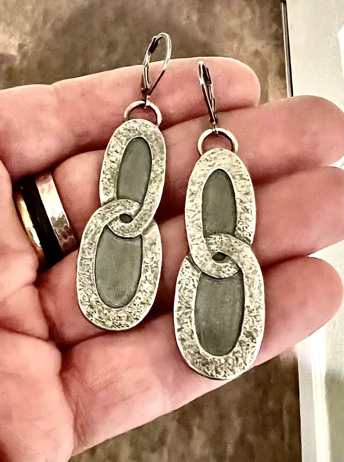 Pair of silver metalsmith earrings with textured frames and dark stone inlays, held in hand.