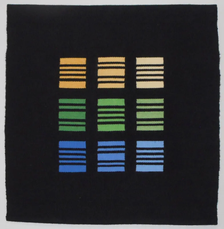 Nine geometric color blocks in gold, green, and blue arranged on a dark woven textile.
