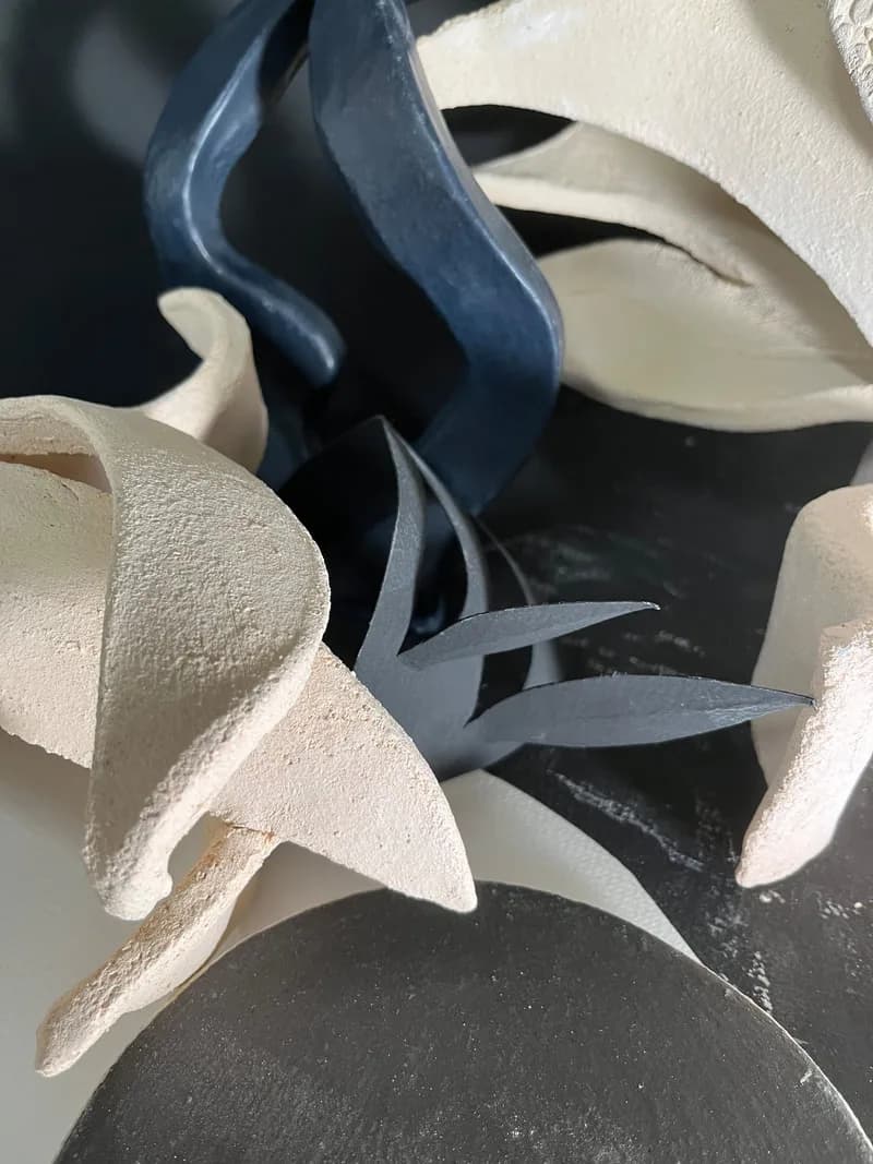 Abstract sculptural forms in cream and dark blue fiber, emphasizing organic curves and spatial interplay.