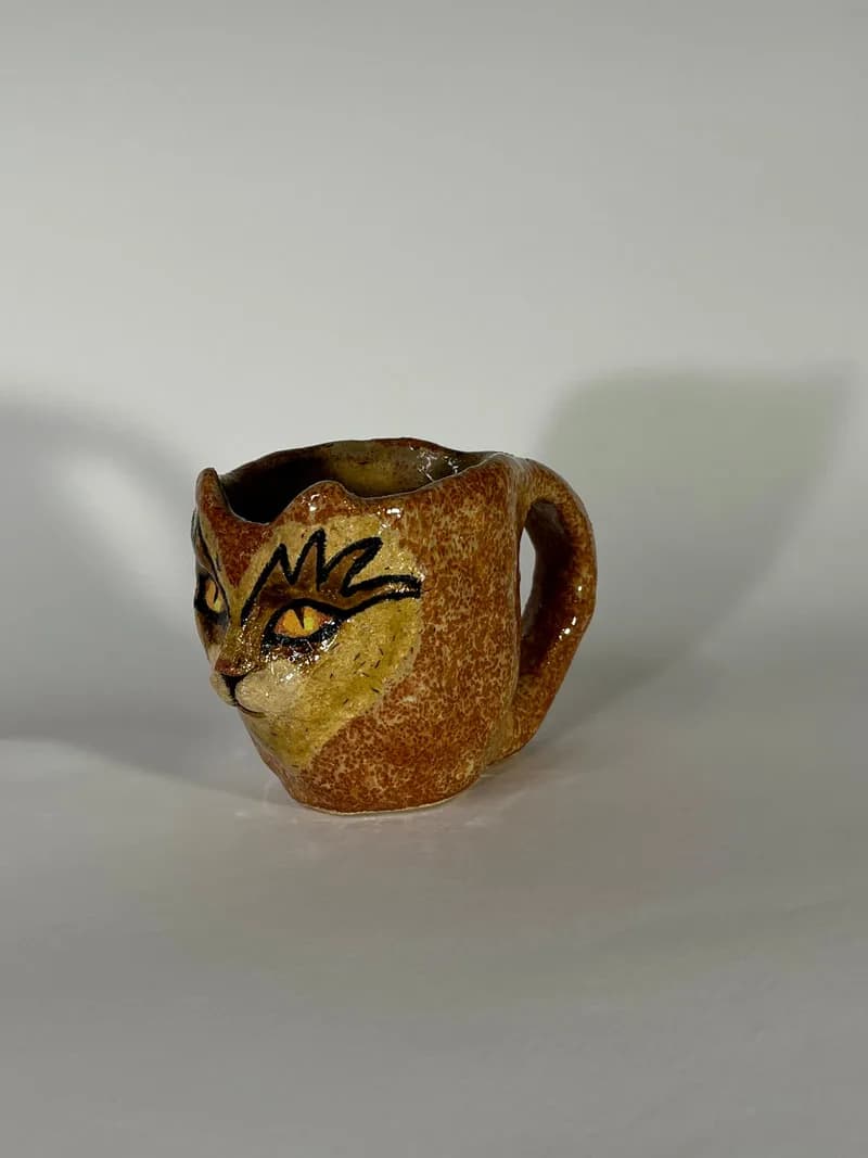 Ceramic vessel with a stylized feline face in ochre and rust glaze.