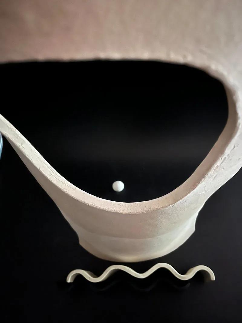 A white ceramic vessel with organic, undulating walls and a sculptural wavy form beside it.