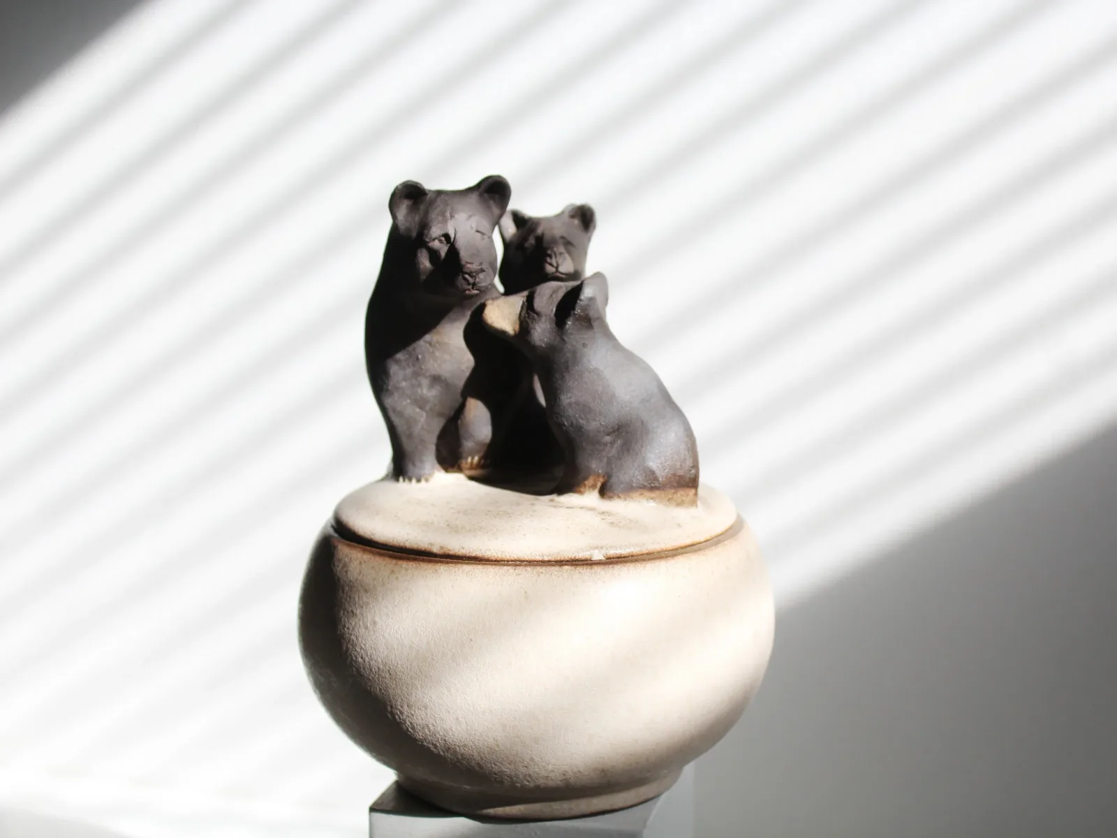 Stone sculpture depicting a mother bear and two cubs emerging from a rounded vessel.