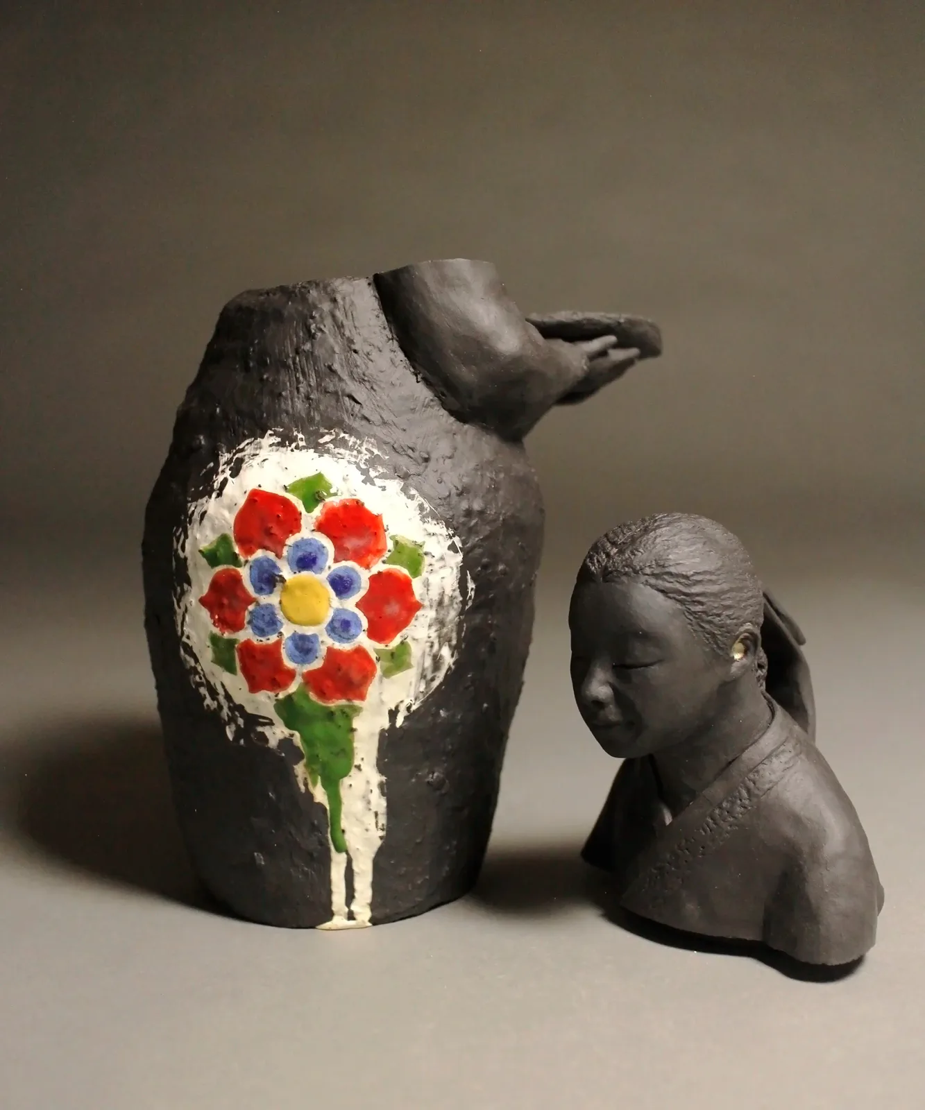 Hand-painted ceramic vessels: a dark clay pitcher with floral motif and a sculpted head form.