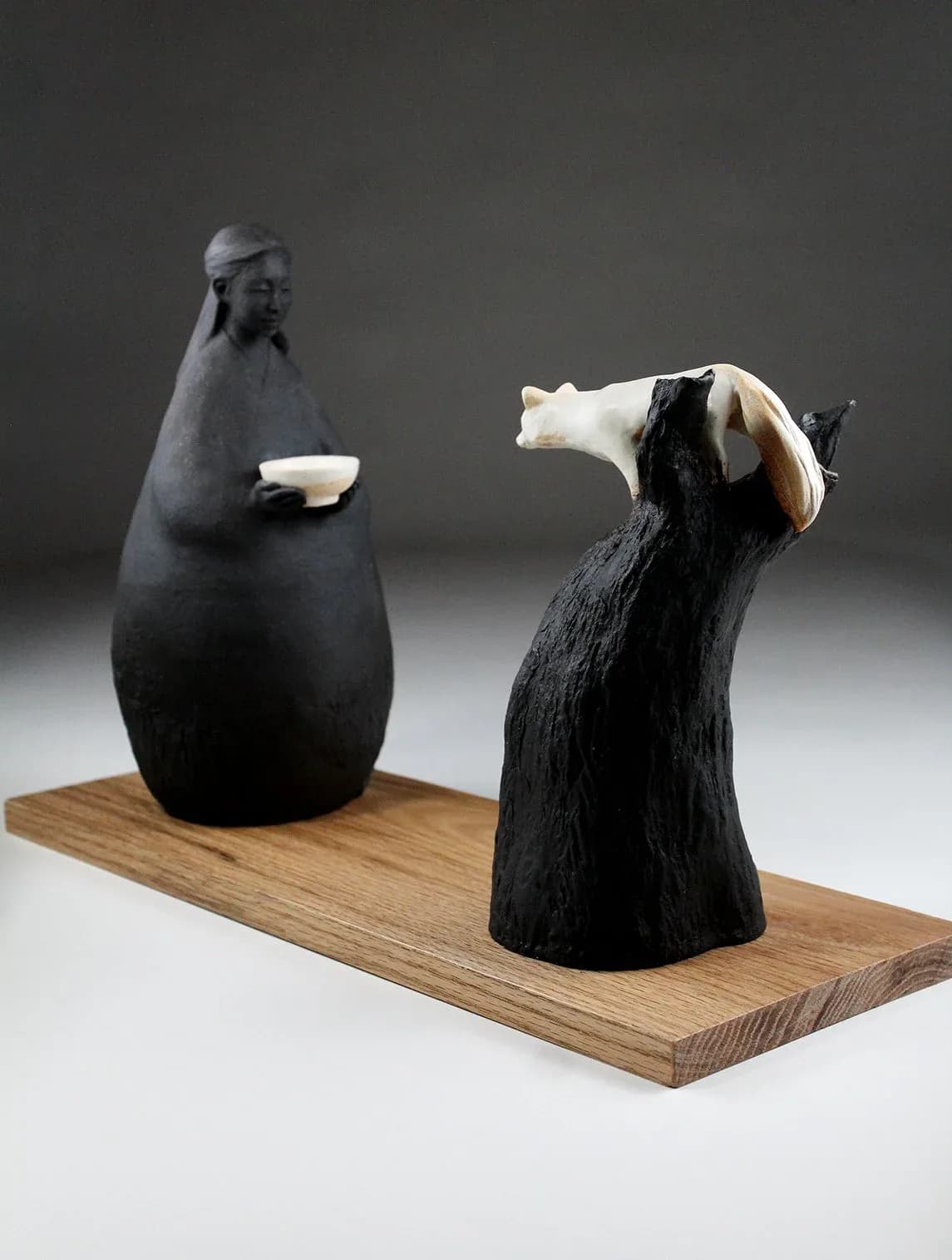 Two figurative wooden sculptures on a wooden base, carved with expressive heads and contrasting light materials.