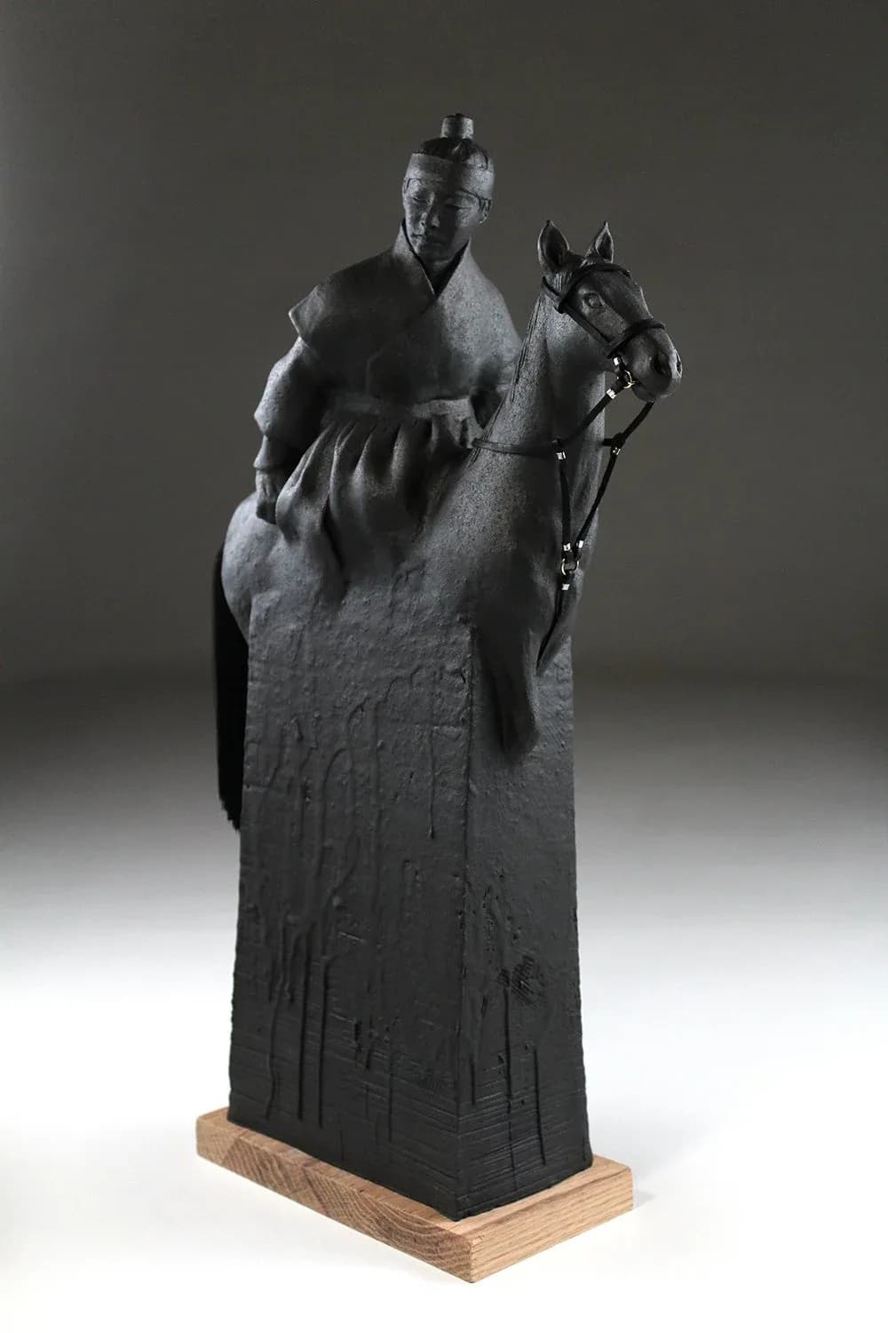 Carved wood sculpture depicting a figure with a horse, rendered in dark finish on a wooden base.
