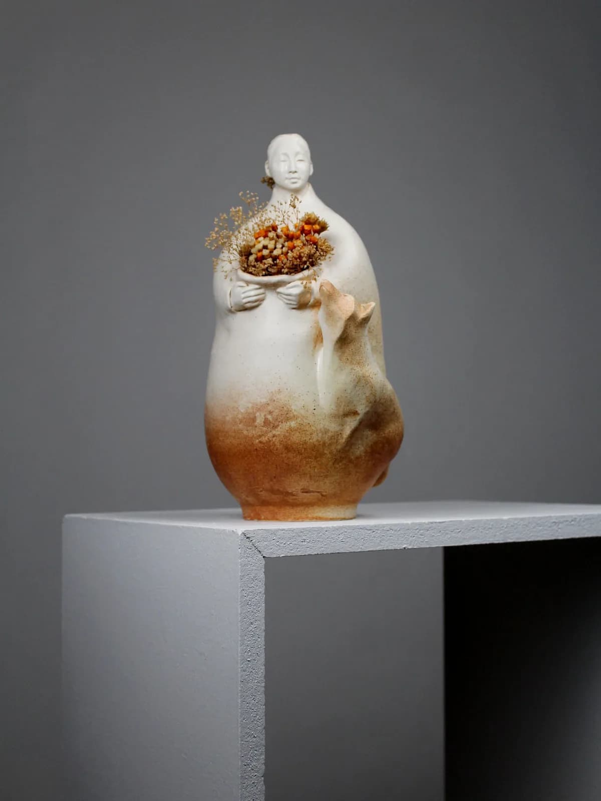 Ceramic and mixed-media sculptural figure holding dried florals and seeds.