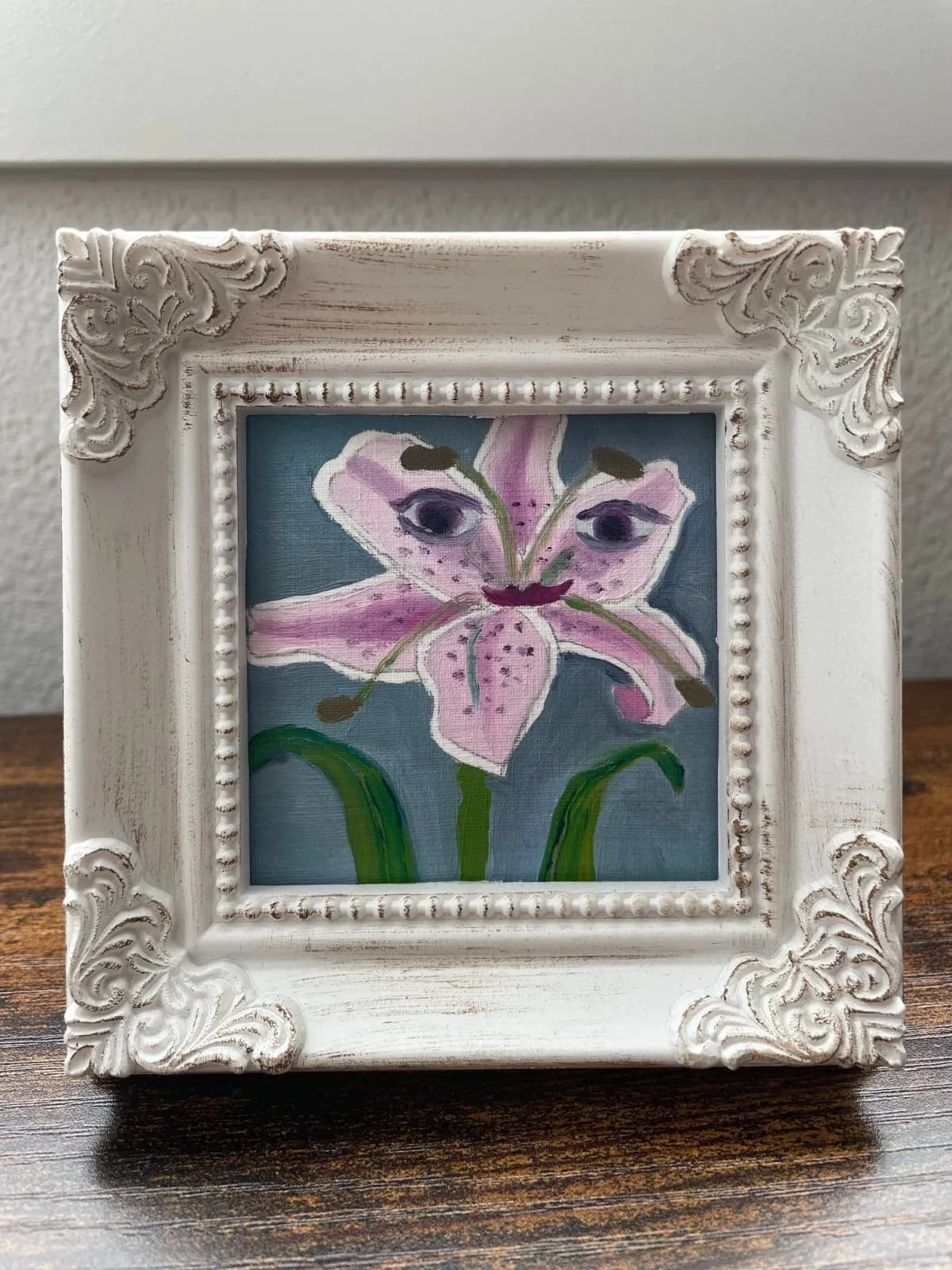 Oil painting of a pink orchid with green stems in an ornate white frame.