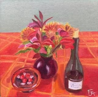 Still life arrangement with red flowers, wine bottle, and dark bowl on coral-red draped fabric.