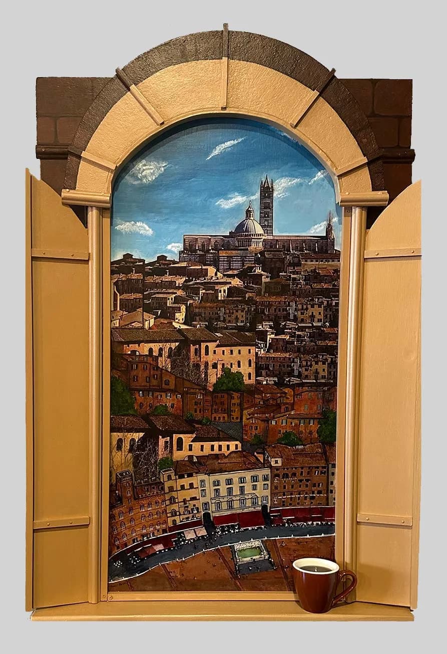 A painted Tuscan cityscape viewed through a wooden arched window and open yellow doors, with a ceramic mug below.
