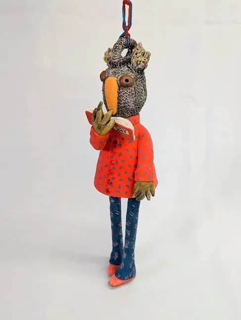 A whimsical fabric bird figurine in a red polka-dot coat and blue legs hangs from a braided cord.