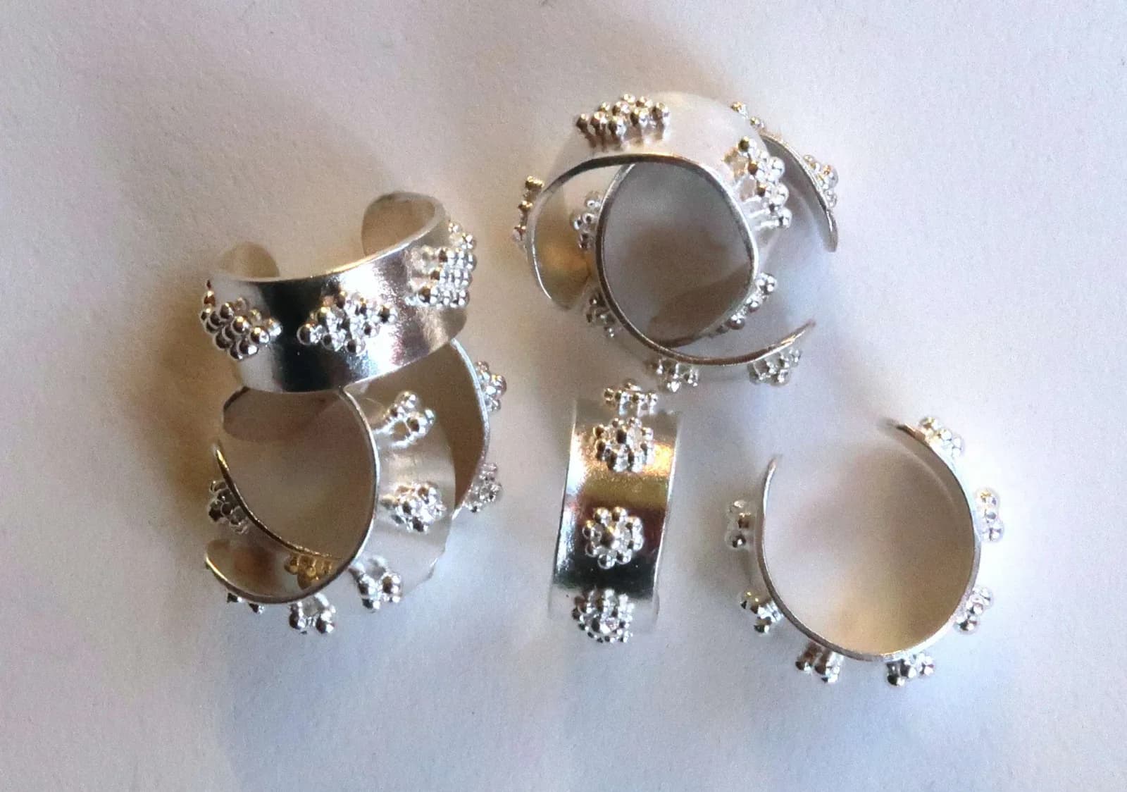 Three contemporary metal rings and bracelets with set stones and textured silver details.