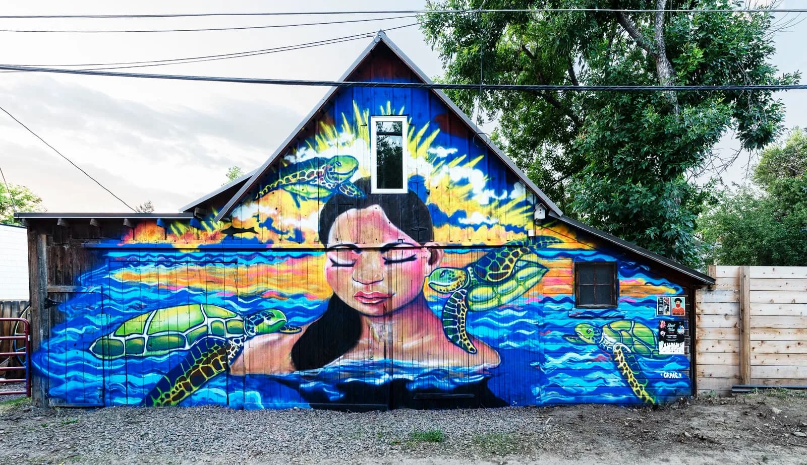 A colorful mural depicts a figure swimming with sea turtles in a vibrant underwater scene painted on a garage wall.