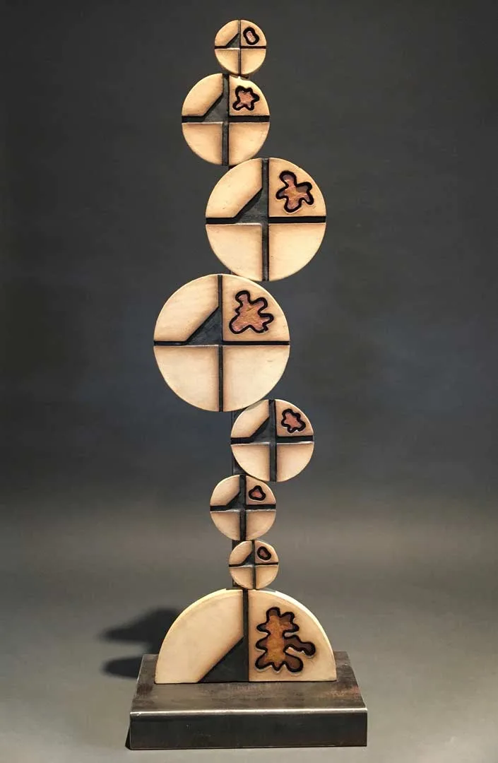 Stacked wooden spheres bisected by vertical lines, incised with stylized figures, mounted on a dark base.