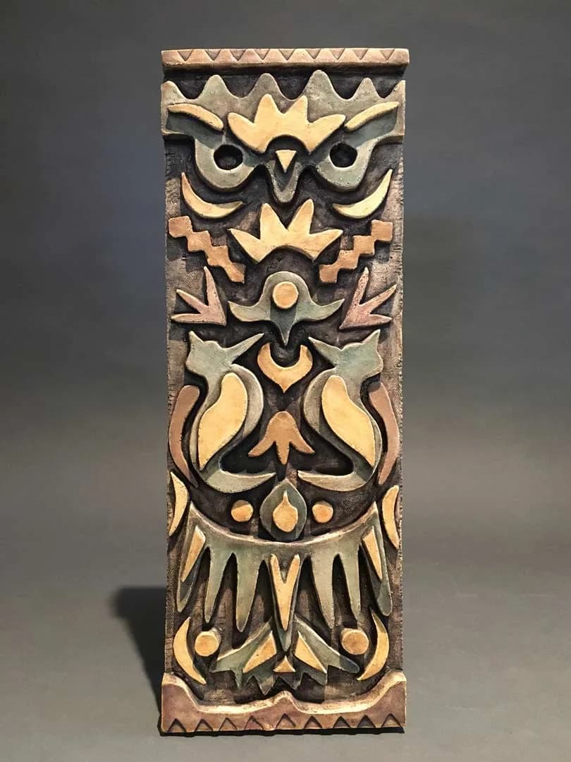 Carved wood sculptural panel featuring stacked owl faces with geometric and floral motifs in folk-art style.