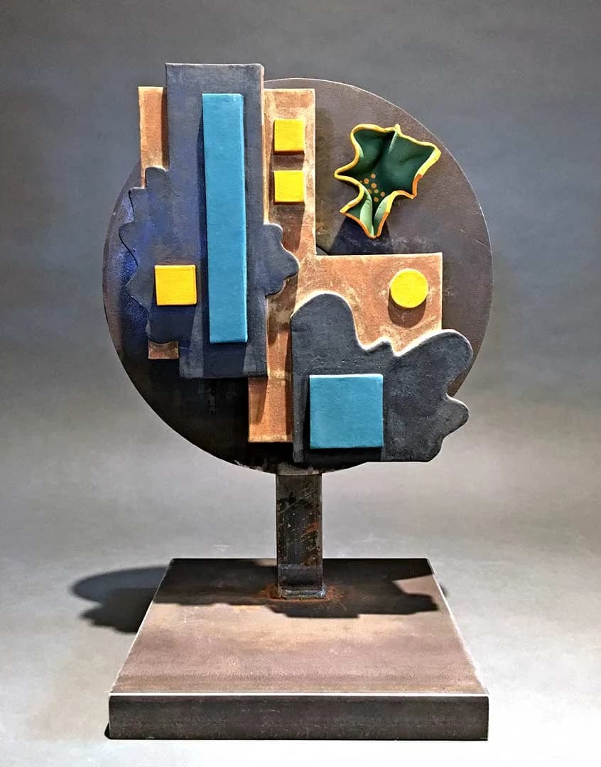 Abstract metal sculpture with geometric forms and colorful enameled accents mounted on a pedestal.