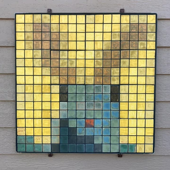 Non-representational glass mosaic with yellow, blue-green, and brown tiles set in a dark grid frame.