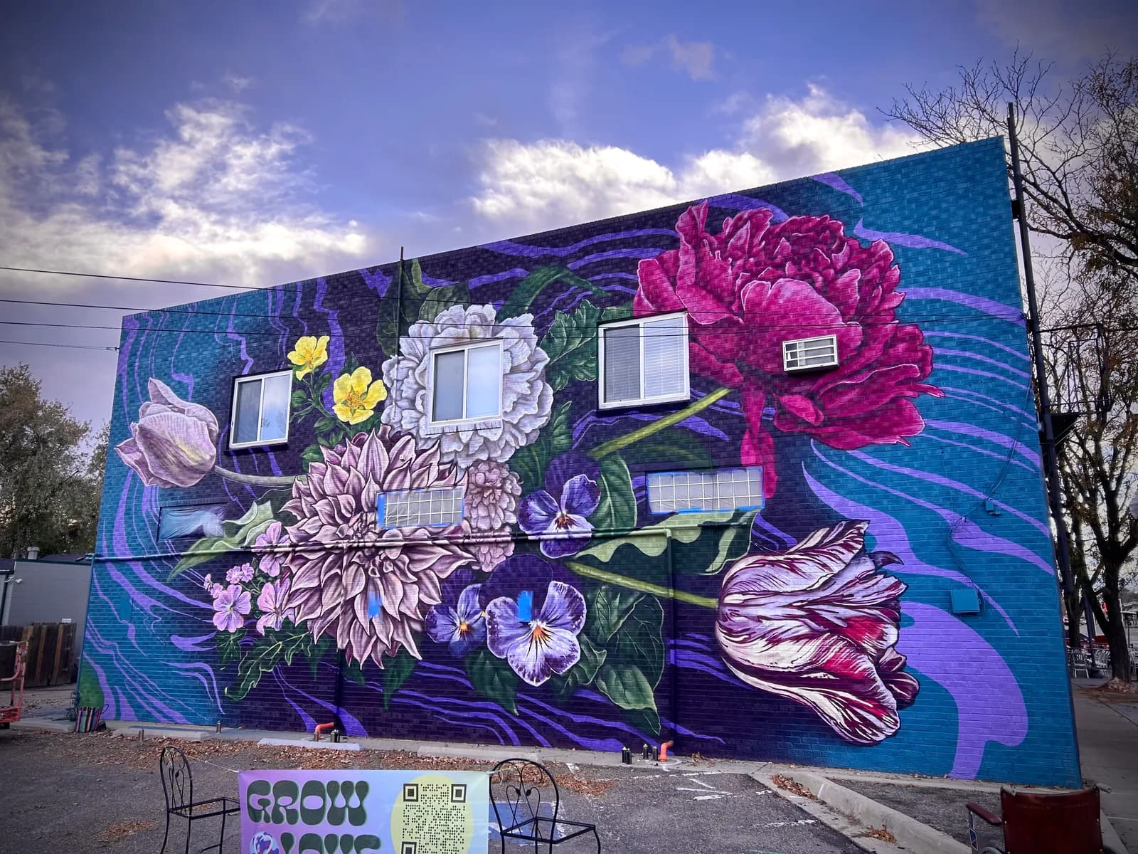 Large-scale mural depicting vibrant pink, purple, and yellow flowers painted on a blue building facade.
