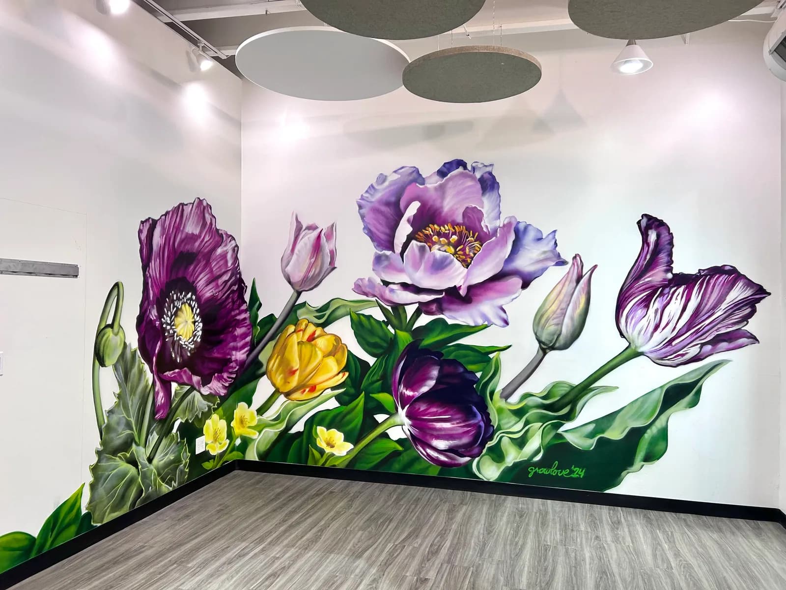 Large-scale mural of purple, pink, and yellow flowers with green foliage rendered in acrylic on an interior wall.