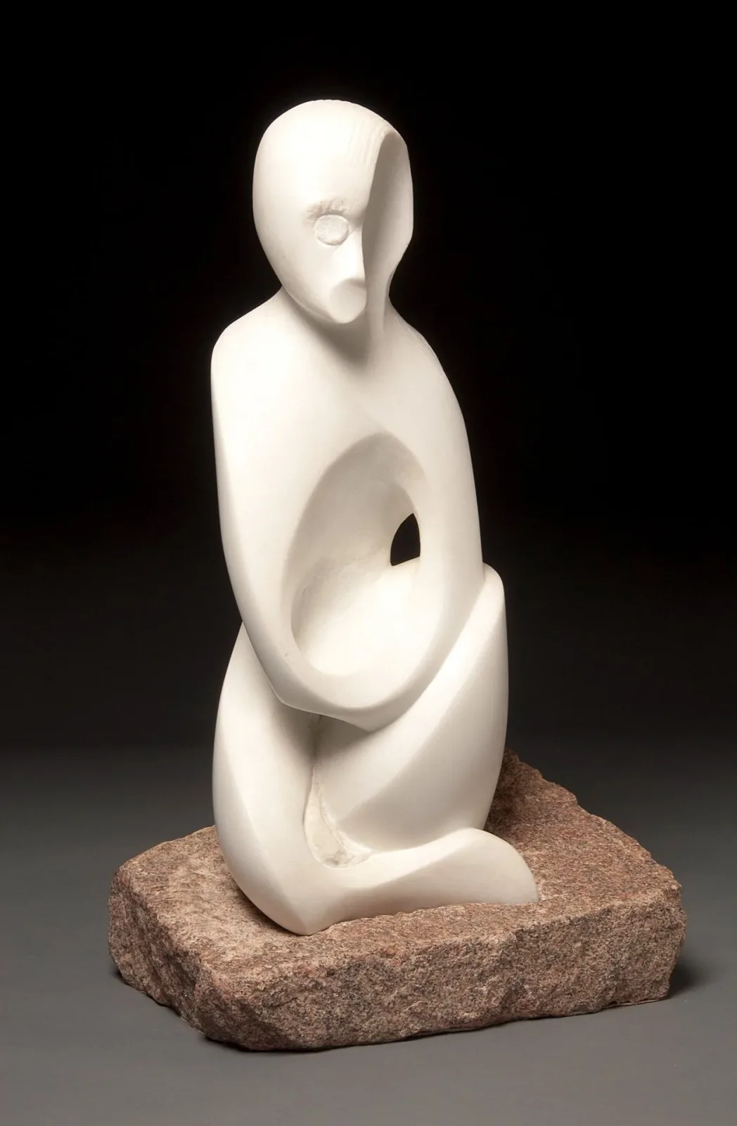 Abstract carved stone figure with organic voids and flowing form on granite base.