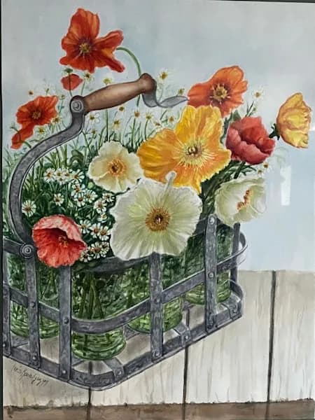 Red and yellow flowers overflow from a vintage metal watering can on a whitewashed wooden surface.
