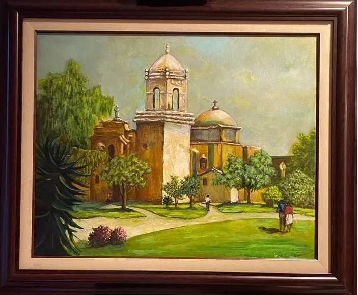 A Spanish mission church with golden domes and bell tower stands amid landscaped grounds with figures and flowering plants.