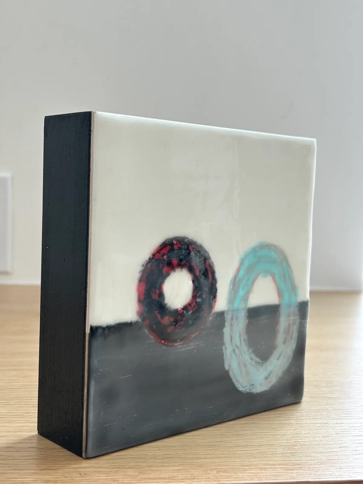 Abstract oil painting with two circular forms in red and turquoise on a divided cream and gray ground.