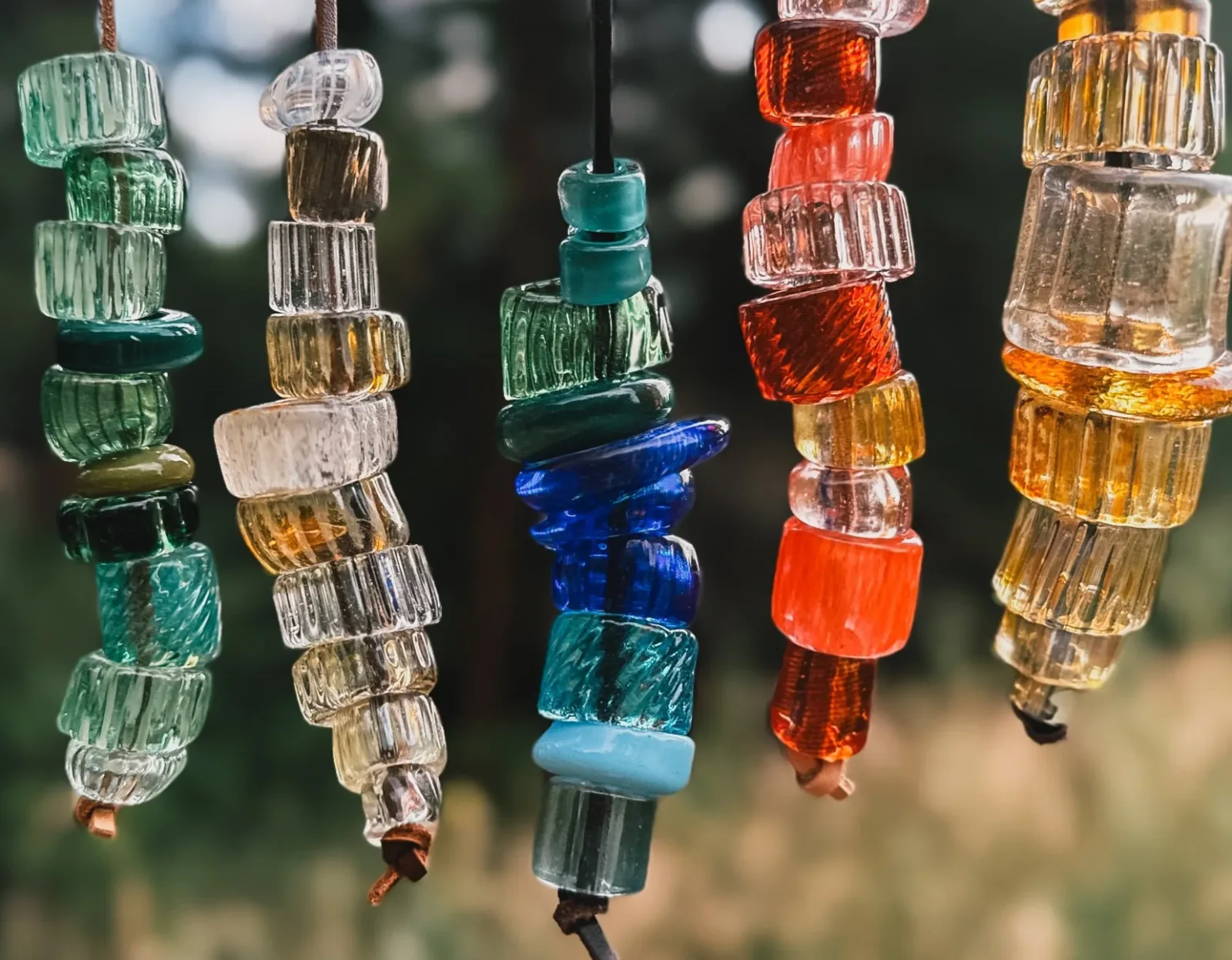Stacked translucent glass beads in green, amber, and red suspended on cordage, catching light.
