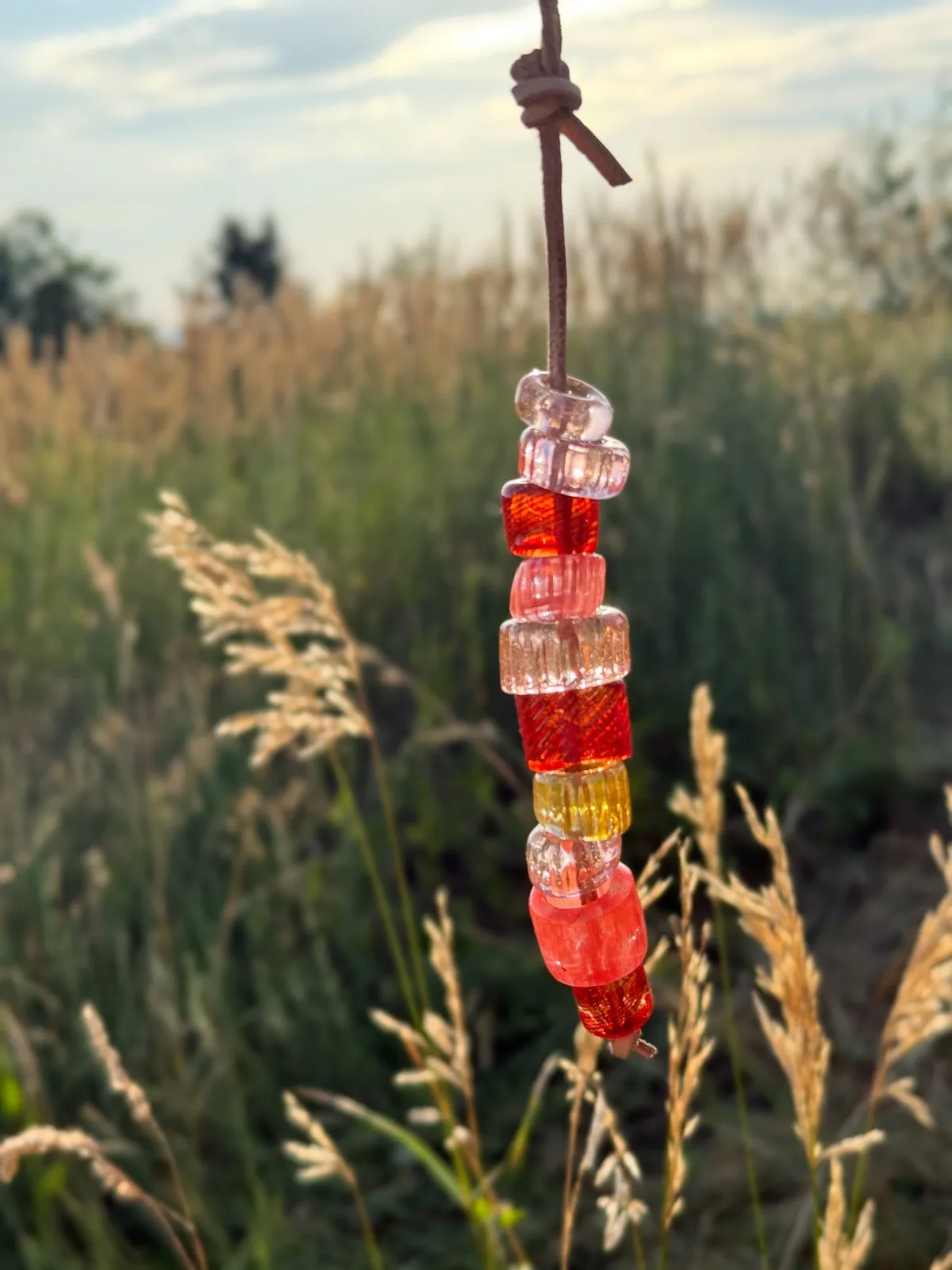 Hand-beaded glass pendant with Valencia, red, and golden tones suspended on leather cord in Colorado foothills.