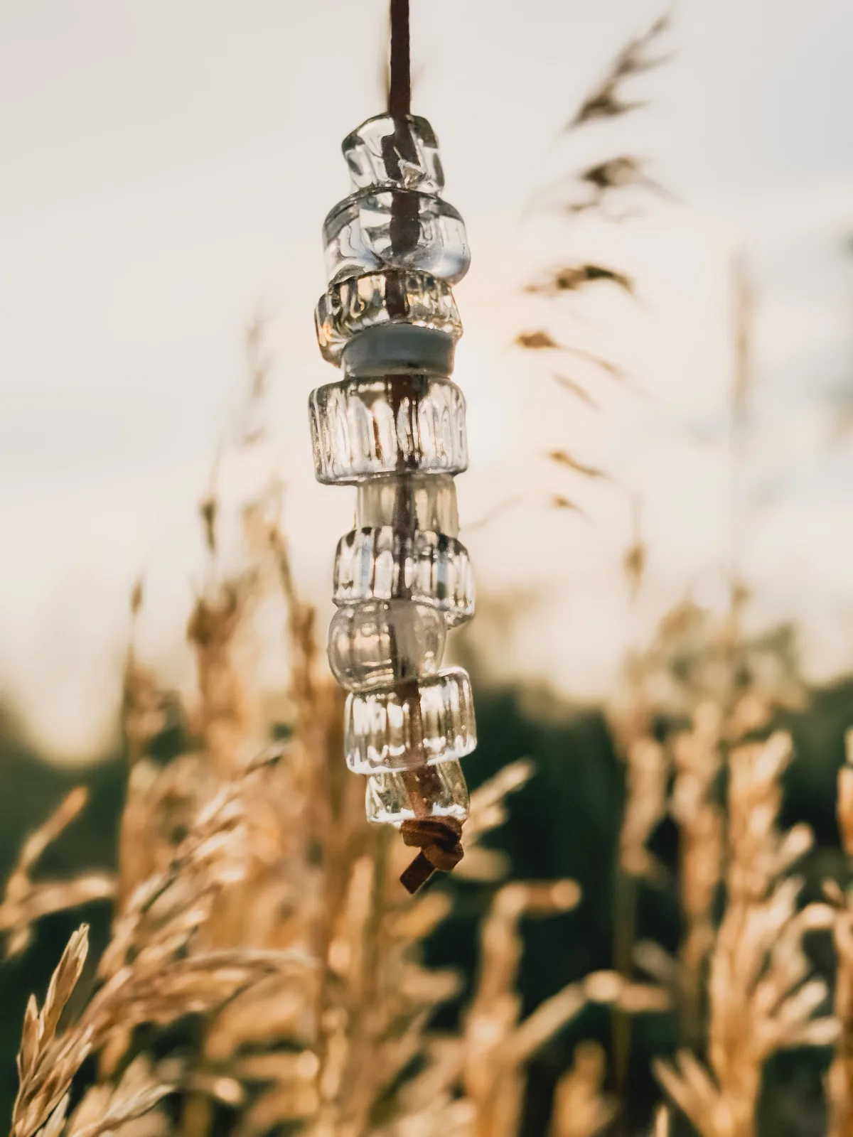 Stacked glass and metal wind chime suspended above dried grasses and foliage.