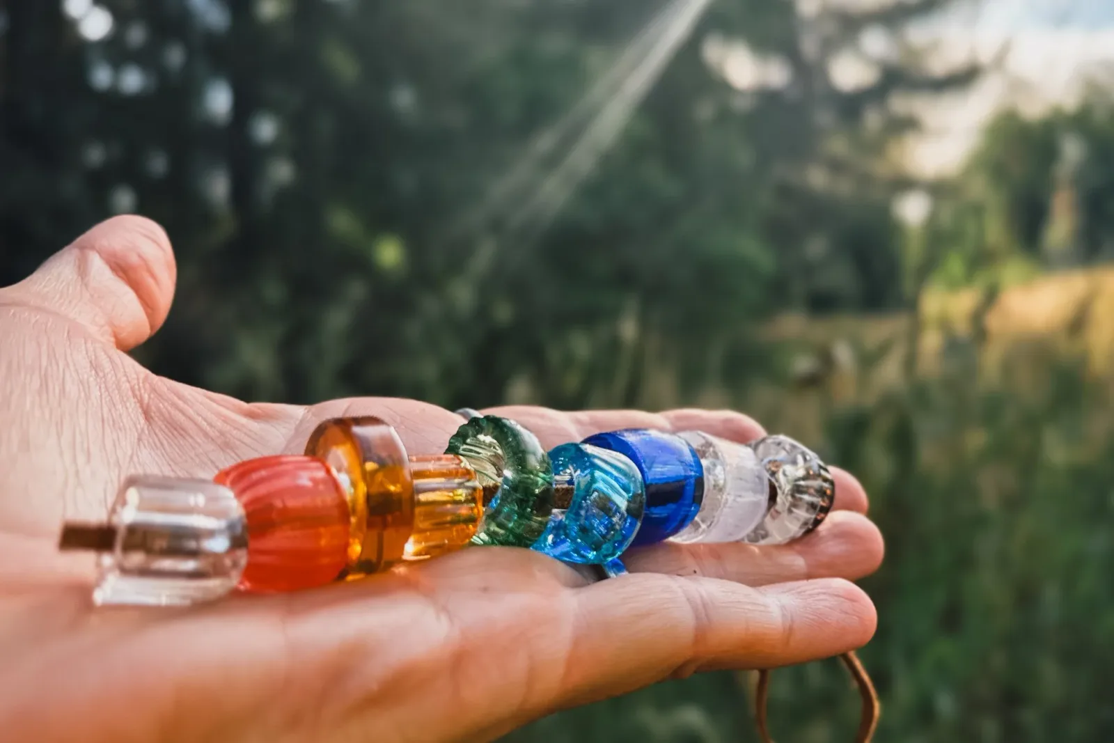 A series of translucent glass beads in red, amber, green, blue, and clear displayed in an artist's hand.