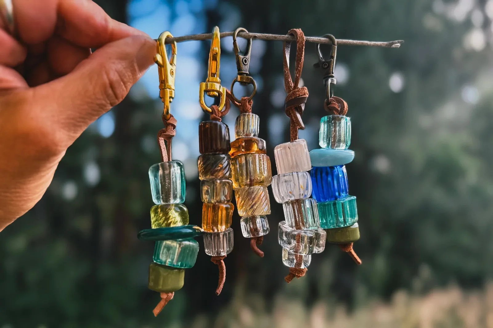 Five glass and metal earrings with beads and wire displayed on a stick in natural light.