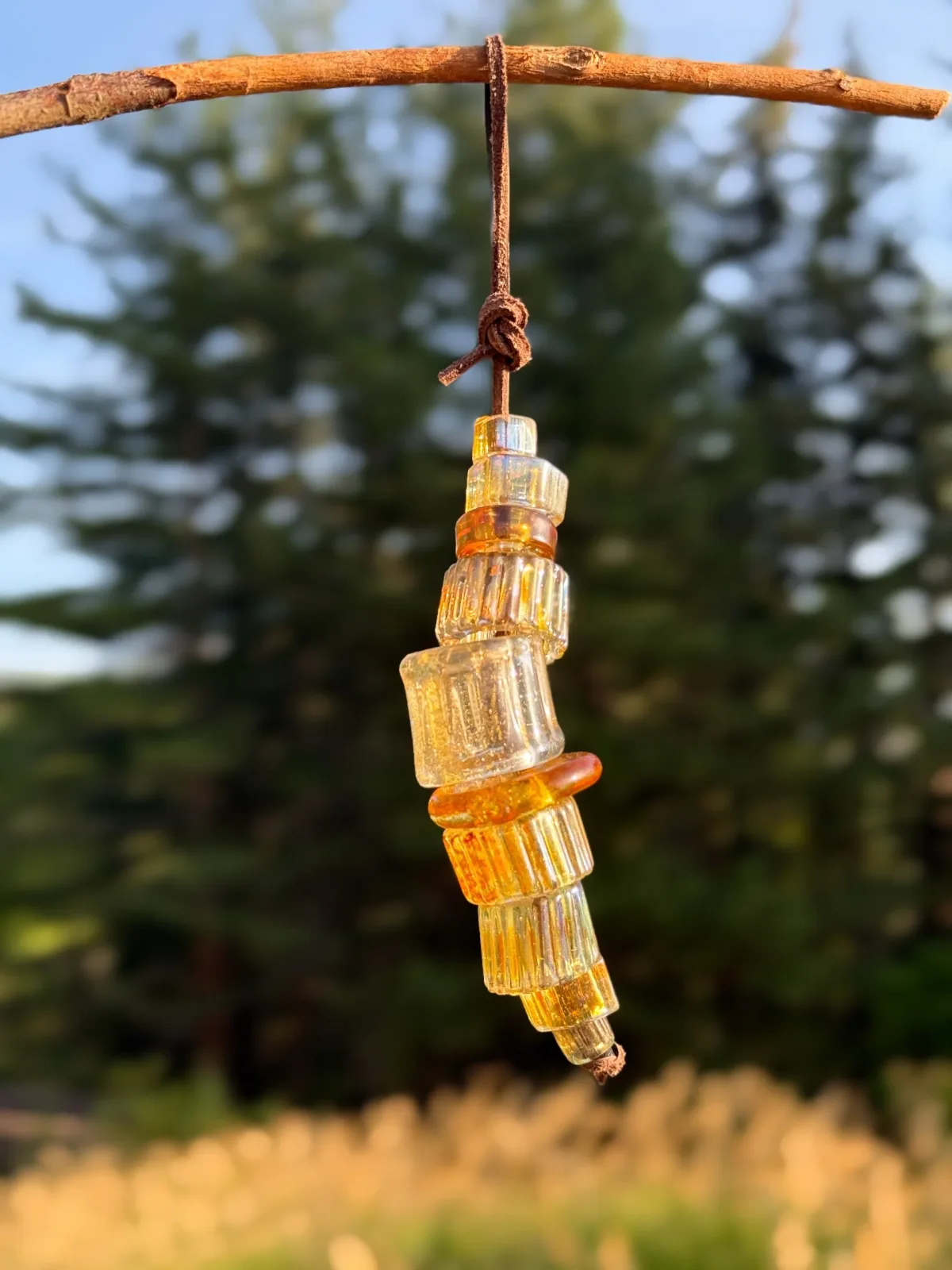 Stacked amber and clear glass segments suspended by cord from a weathered branch.