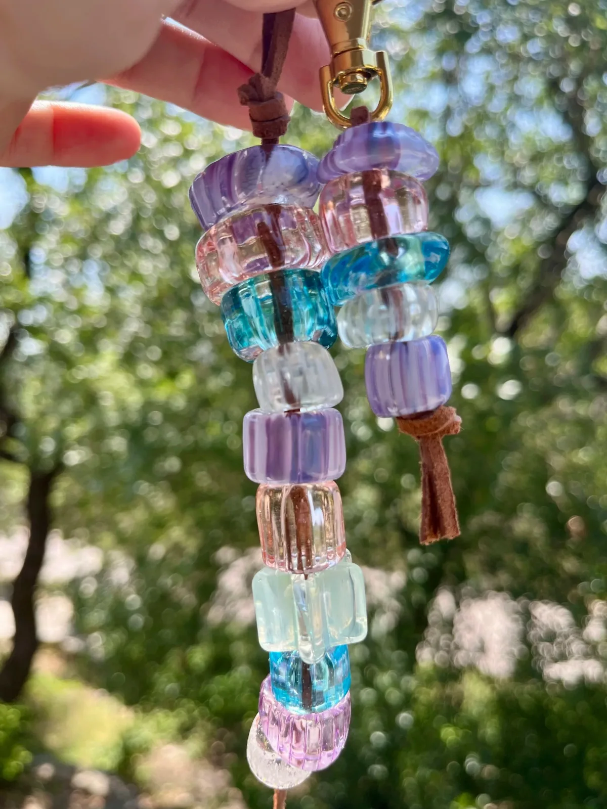 Stacked glass bead pendant in Opium, Buccaneer, Celeste, and clear tones suspended from a cord.
