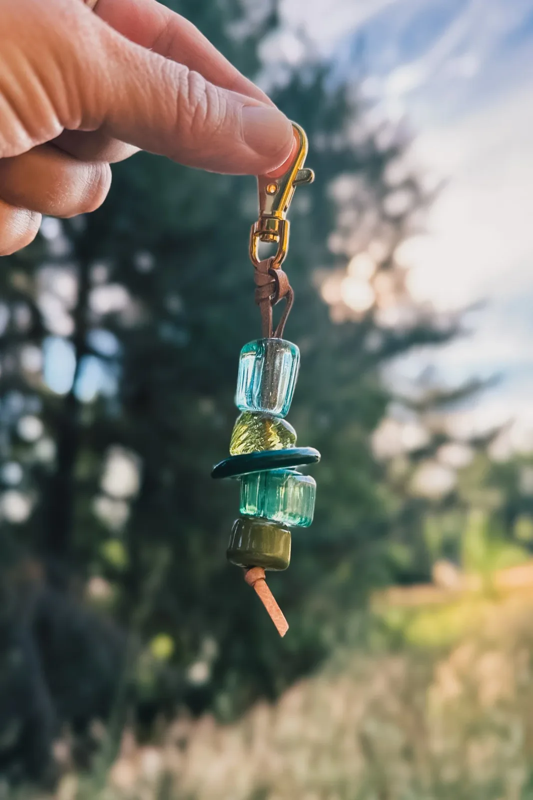 Stacked glass gemstone keychain with brass hardware, held against a conifer backdrop.